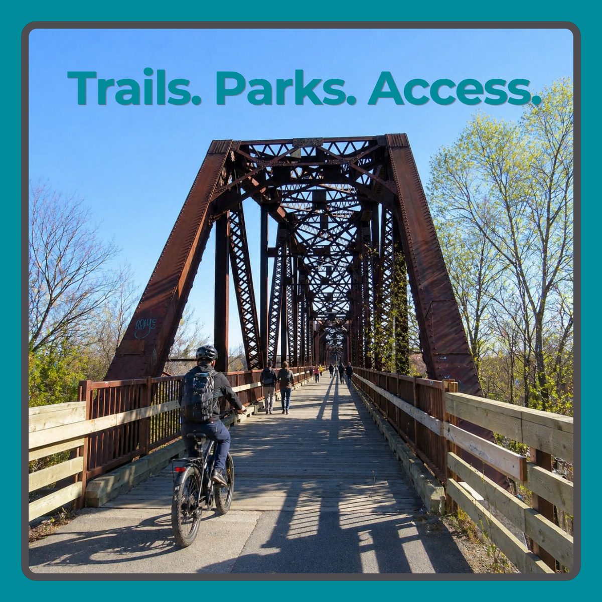 Cyclist and pedestrians using a Fredericton trail bridge during spring, showing how trails, bridge access, and infrastructure affect daily life and real estate decisions.
